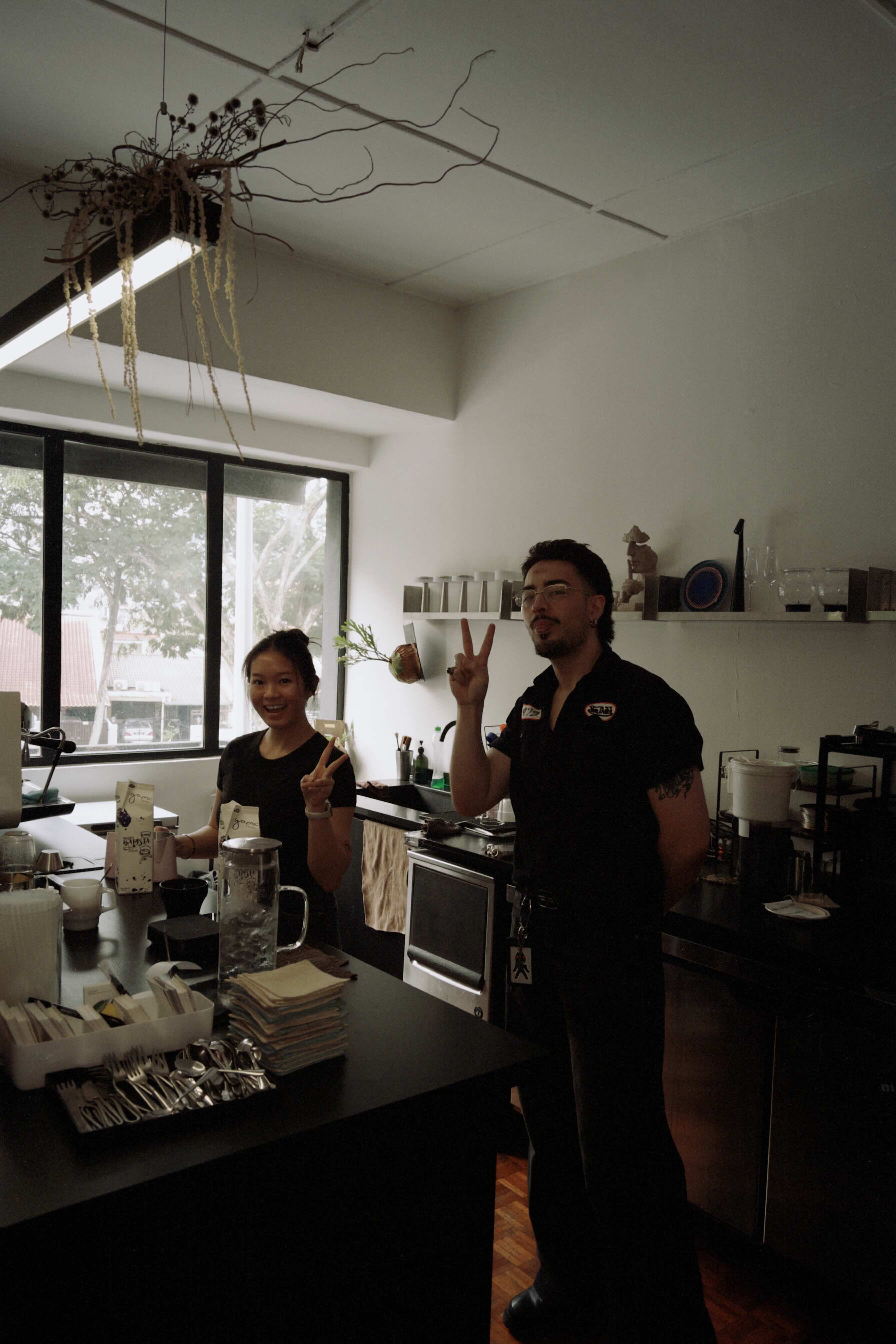 Two people in a kitchen with a shelf and window in the background
