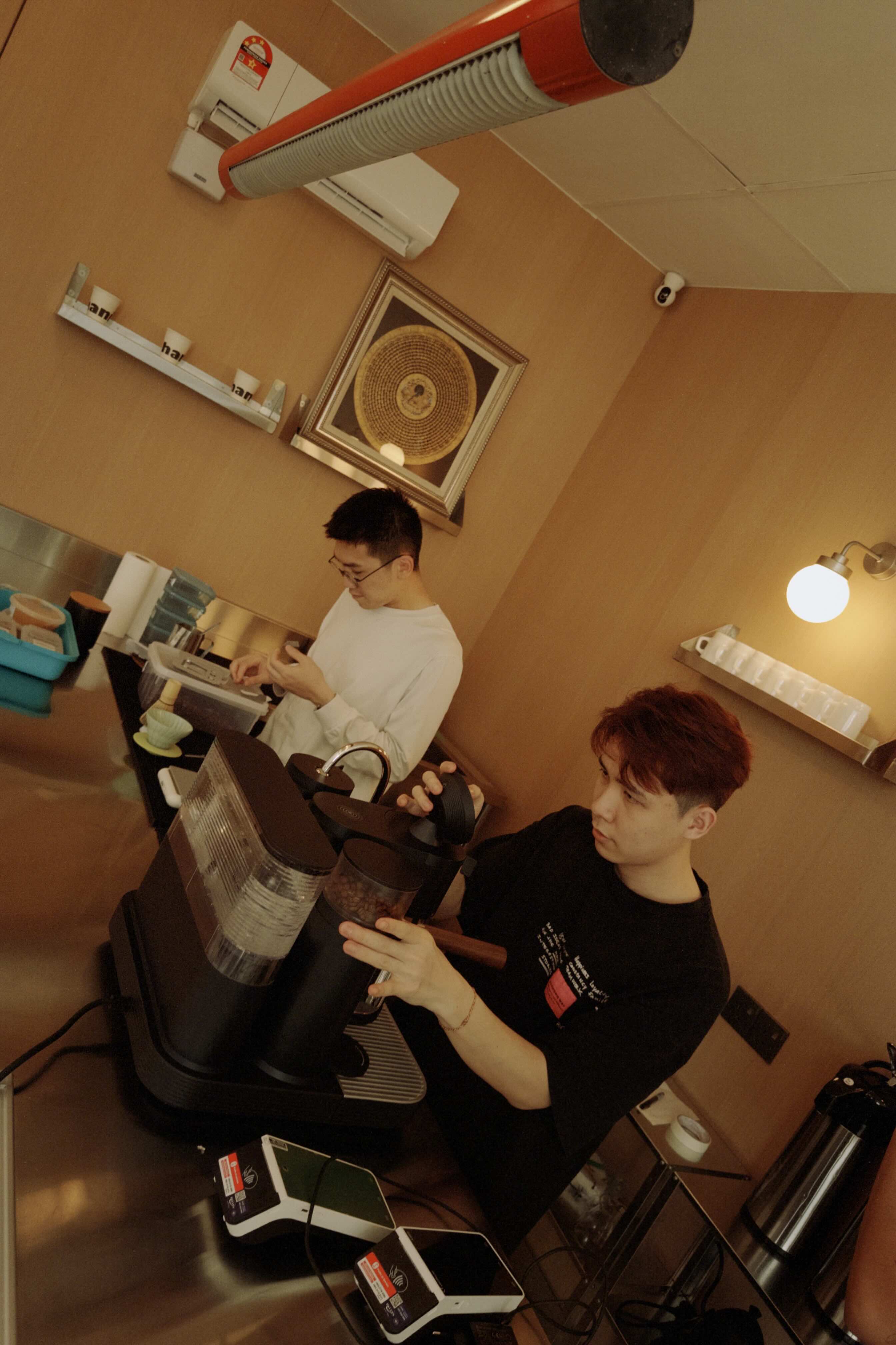 Two baristas working in a coffee shop with equipment and decor.