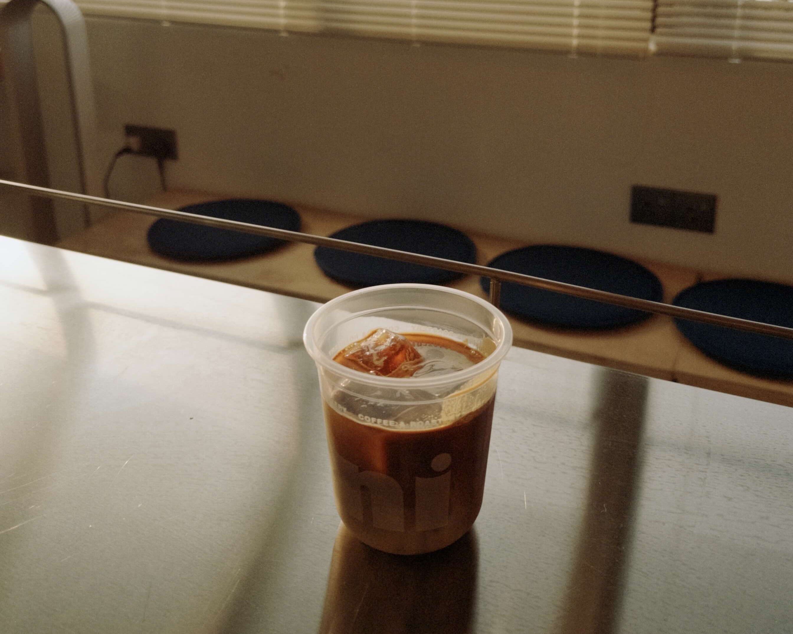 Clear plastic cup with a dark liquid on a reflective surface with blinds in the background