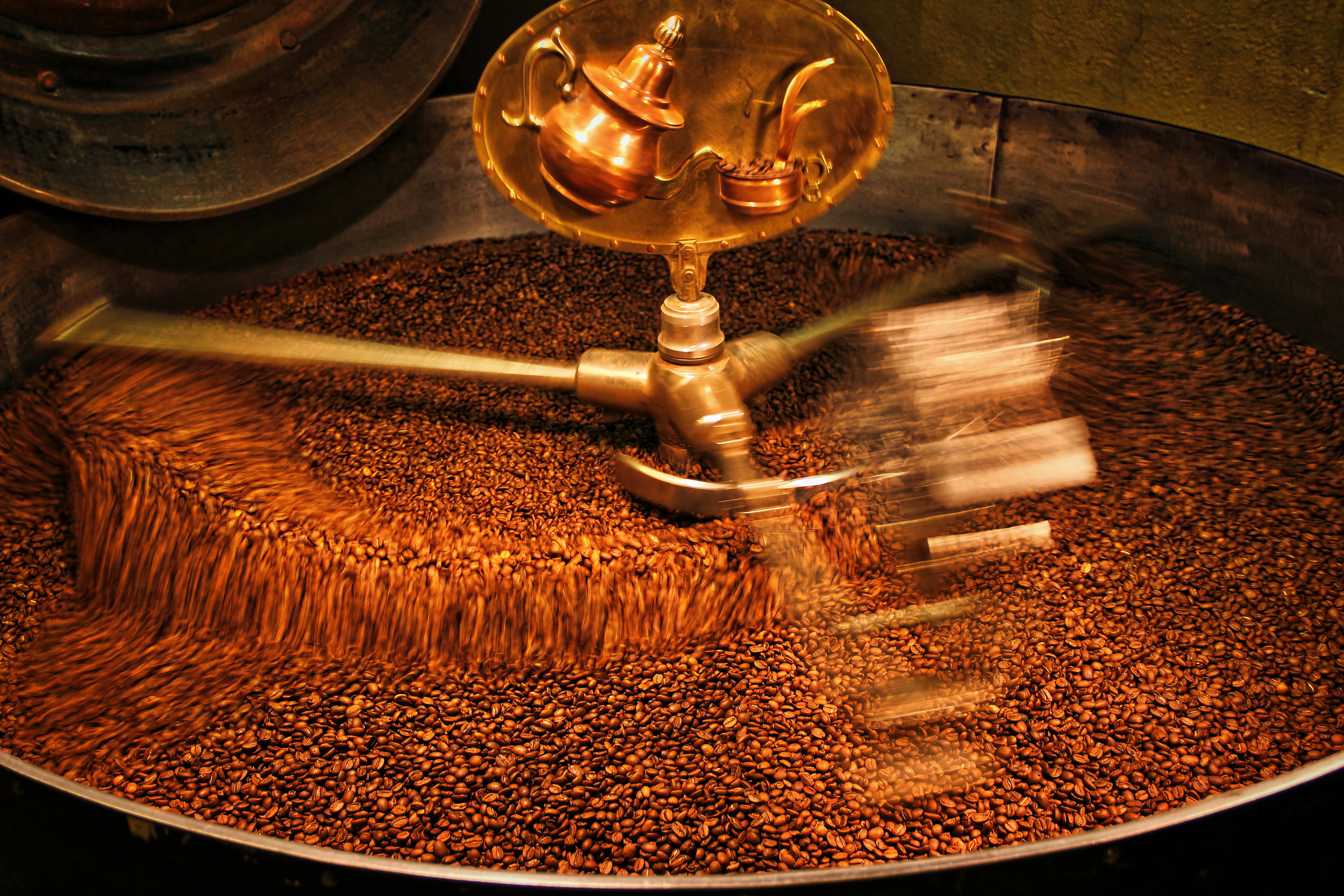 Coffee beans being roasted in a large metal roaster with a golden valve.